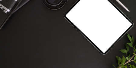 Top view of dark modern workplace with blank screen tablet, office supplies and copy space on black...