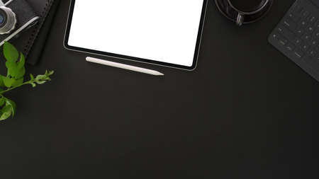 Top view of dark stylish workplace with mock up tablet and office supplies on dark table background 