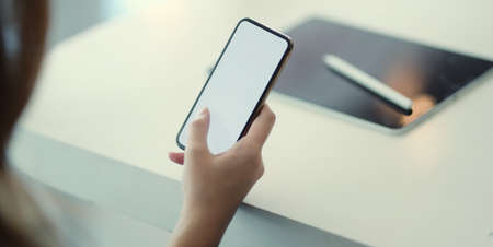 Close-up view of young businesswoman using blank screen smartphone while working on the project in office room の写真素材
