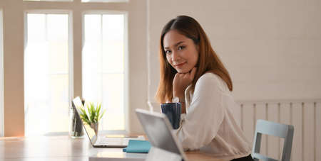 Portrait of beautiful businesswoman working with laptop computer and smiling to the camera in modern...