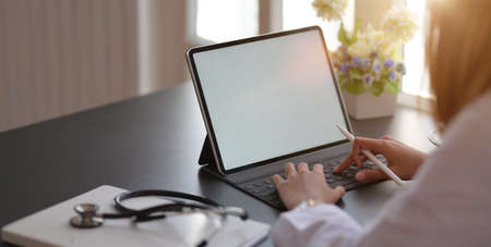 Cropped shot fo young female doctor working on medical records and exam results with tablet in...