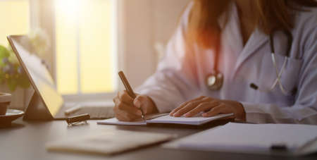 Close-up view of young female doctor writing medical charts with tablet in her office room