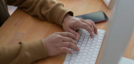 Close-up view of young man typing on keyboard computer while working on his project