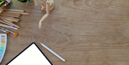 Top view of comfortable artist workplace with painting tools and tablet on wooden table
