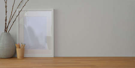 Cropped shot of workplace with mock up frame and office supplies on wooden table and white wall...