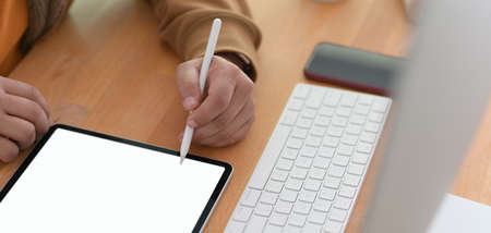 Close-up view of young man working on his project with blank screen tablet in comfortable office...