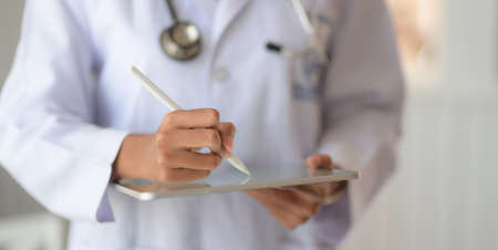 Cropped shot of young doctor checking patient chart while using digital tablet in the hospital