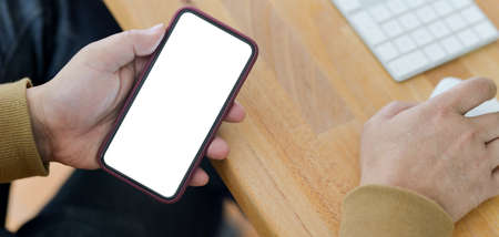 Close-up view of young man holding blank screen smartphone in comfortable office room 