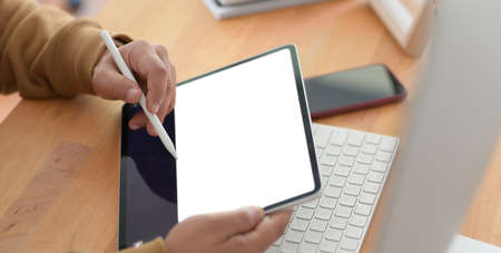 Close-up view of young man working on his project with blank screen tablet in comfortable office...