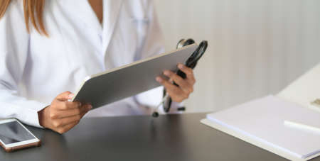 Cropped shot of young female doctor reading medical charts with tablet in modern office roomの写真素材