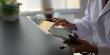 Young female doctor analysing medical charts with tablet in modern office roomの写真素材