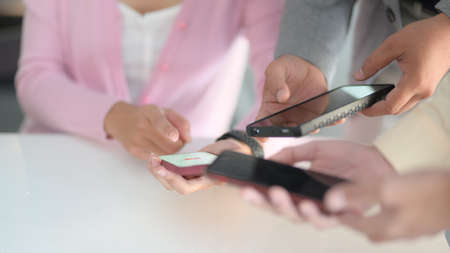 Cropped shot of young business people discussing the project while using smartphone in office room