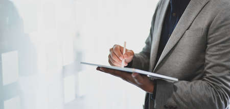 Cropped shot of young businessman using tablet while working on his project in office roomの写真素材