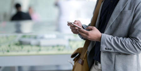 Close-up view of young businessman using smartphone with blurred office room backgroundの写真素材