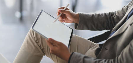 Cropped shot of young businessman working on his project while using digital tablet in modern office...