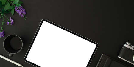 Top view of trendy photographer workplace with blank screen tablet and office supplies on black...
