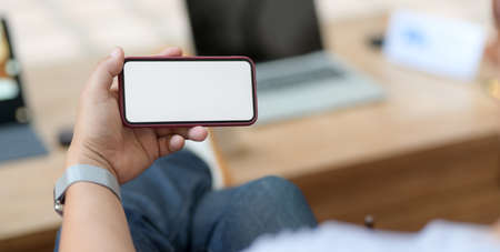 Cropped shot of young man holding blank screen smartphone while sitting in comfortable workplace