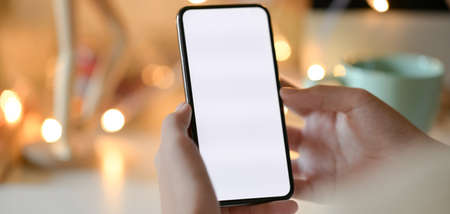 Cropped shot of businesswoman holding blank screen smartphone in workplace with bokeh light...