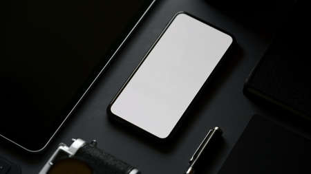 Cropped shot of blank screen smartphone in dark modern office room の写真素材