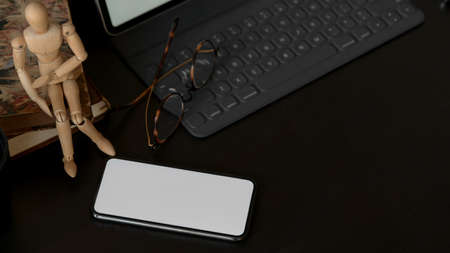 Cropped shot of blank screen smartphone in dark modern office room 