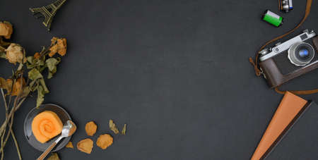Top view of dark vintage workplace with office supplies and orange jam rolls on black table...