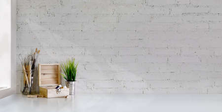 Cropped shot of minimal artist workplace with painting tools on white table and white brick wall...