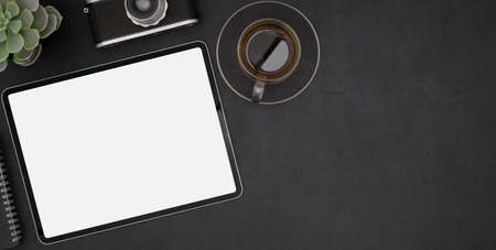Top view of dark modern workplace with blank screen tablet and black coffee cup on black desk...