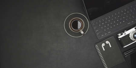 Top view of dark modern workplace with tablet, coffee cup and office supplies on black desk backgroundの写真素材