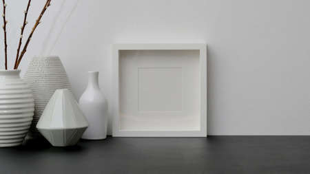 Close up view of modern workspace with frame and ceramic vase on black desk with white wall backgroundの写真素材