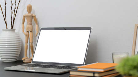Close up view of modern workspace with mock up laptop, wooden figure, books and decorations on black desk with white wall backgroundの写真素材