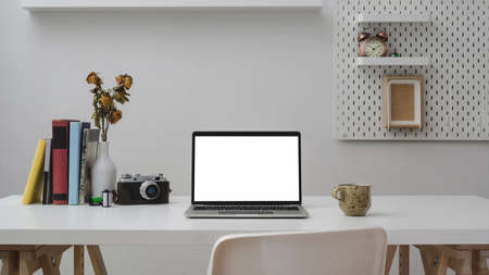Close up view of modern office room with blank screen laptop, office supplies, camera, coffee cup and decorations on white wooden table with white wallの写真素材