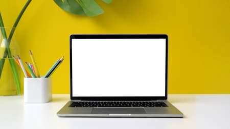 Close up view of colorful workspace with blank screen laptop, pencils and vase on white table with...