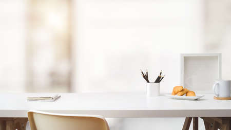 Close up view of simple workspace with copy space, frame, stationery, coffee cup and croissant on white table with blurred backgroundの写真素材