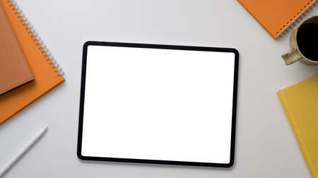 Top up view of trendy workplace with mock up tablet, office supplies and coffee cup on white table...