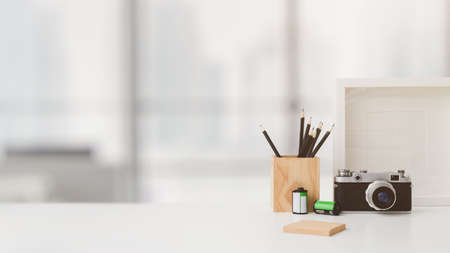Cropped shot of photographer workspace with copy space, camera, stationery, mock up frame, and tree pot on white table with blurred backgroundの写真素材