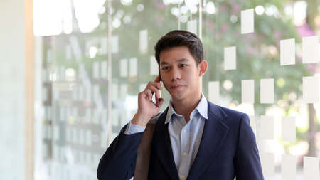 Close up view of young professional businessman talking on his smartphone in blurred meeting room background の写真素材