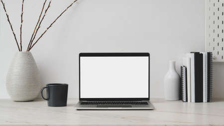 Cropped shot of minimal workplace with blank screen laptop, decorations, books and coffee up on...