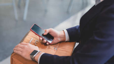 Cropped shot of  professional businessman holding on smartphone while sitting with document bag in...