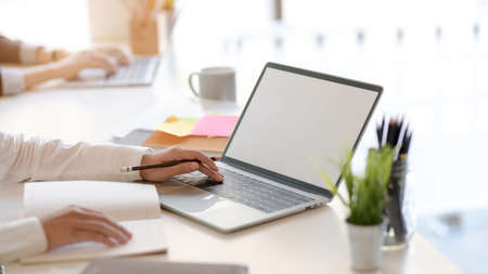 Cropped shot of young professional businessman typing on blank screen laptop and office supplies in...