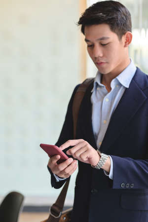 Close up view of young professional businessman using on smartphone while standing in office roomの写真素材