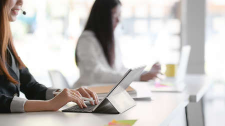 Side view of female customer service sitting in line call centre operation and talking on headset in office roomの写真素材