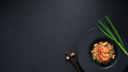 Top view of Pad Thai, stir fly of Thai noodle with shrimp and egg in black ceramic plate with copy space on black table の写真素材