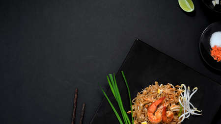 Overhead shot of Pad Thai, stir fly of Thai noodle with shrimp, egg and seasoning in black ceramic plate on black table の写真素材