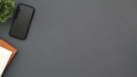 Top view of dark modern workspace with copy space, smartphone, office supplies and tree pot on grey table backgroundの写真素材