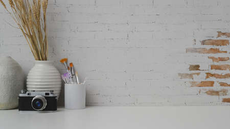Cropped shot of artist workspace with copy space, camera, painting brush and ceramic vases on white...