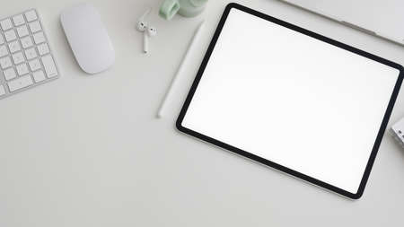 Top view of minimal workspace with  blank screen digital tablet, copy space, computer, laptop and office supplies on white desk backgroundの写真素材