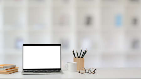 Close up view of trendy home office with blank screen laptop, stationery, glasses and coffee cup on...