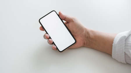 Cropped shot of businessman holding blank screen smartphone in on white table background