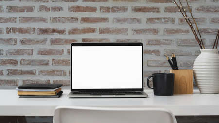 Close up view of contemporary workplace with blank screen laptop, office supplies and decoration on white table with brick wall background の写真素材