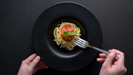 Top view of a woman with fork ready to eat spaghetti in a black plate on black table backgroundの写真素材